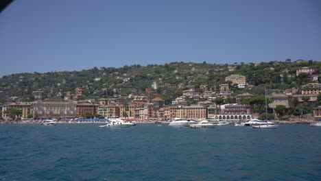 Ferry-boat-navigating-and-sailing-off-the-Ligurian-Sea-in-Portofino,-Italy-and-against-the-background-view-of-the-vibrant-houses-and-boats