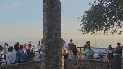 Tourists-group-taking-photos-of-sunset-over-Malaga-port-view-from-hilltop-lookout-Gibralfaro-castle,-Spain
