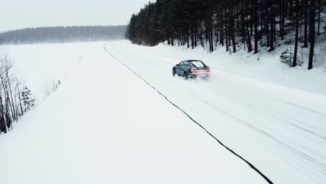 an-electric-car-is-driving-on-a-snow-covered-road-in-the-arctic-circle-during-a-snowfall,-followed-by-a-drone