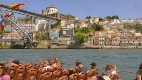 Tourists-On-Boat-Excursion-Looking-At-Iconic-Bridge-Of-Dom-Luis-Over-Douro-River-And-Vila-Nova-de-Gaia-In-Porto,-Portugal
