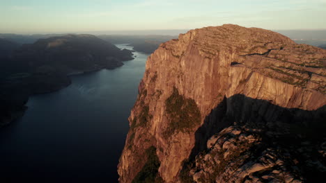 Breathtaking-Aerial-View-of-an-impressive-Cliff-in-Norway,-Sunrise-Atmosphere-in-the-Lysefjorden,-Preikestolen,-Pulpit-Rock,-Some-Tourists-are-Gathered-on-the-Rock