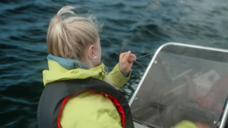 Close-Up-of-A-Pretty-Girl-Fishing-on-a-Small-Motor-Boat-on-a-Beautiful-Fjord-in-Southern-Norway,-Amateur-Fishing,-Girl-Hauling-Back-the-Fishing-Line