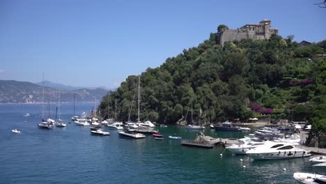 Castello-Brown,-a-historic-castle-perched-on-a-hill-overlooking-the-village-and-boats-sailing-and-mooring-in-the-small-harbour-of-Portofino,-Italy