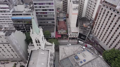 Urban-aerial-pulls-up-from-old-building-surrounded-by-tall-skyscrapers