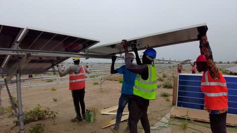 Men-Carefully-Placing-Bifacial-Solar-Photovoltaic-Panel-Over-Steel-Frames-At-The-Solar-Farm-Project-In-Gambia,-West-Africa