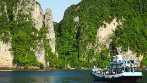 Local-boat-floating-near-massive-vegetated-karst-mountains,-Thailand