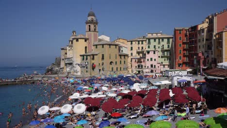 Iconic-view-of-the-famous-Basilica-of-Santa-Maria-Assunta-Church,-tourists-sunbathe,-play-water-activities-and-soak-in-the-warm-Mediterranean-sun-in-Camogli,-Italy