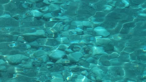 Turquoise-seawater-seascape,-crystal-clean-fresh-green-emerald-sea-water-background-on-pebble-beach,-glittering-aqua-reflecting,-summertime-in-Mediterranean