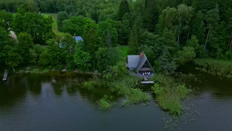 Drone-view-of-house-on-a-pond-nestled-by-green-trees,-flying-closer