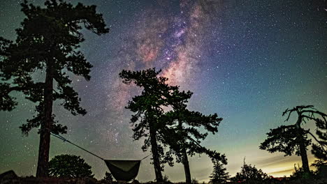 Timelapse-Captures-Milky-Way's-Passage-Across-the-Sky,-Silhouetted-Trees,-and-a-Swinging-Hammock