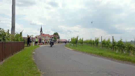 Stunning-HD-footage-of-cyclists-participating-in-a-tour-of-Slovenia,-pedaling-through-Svetinje-and-vineyards,-while-cheerful-children-along-the-road-cheer-them-on