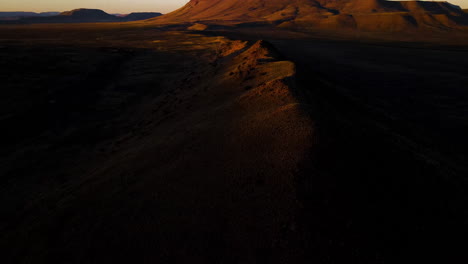 Mountain-tops-highlighted-by-sunset-in-semi-arid-desert-region,-drone