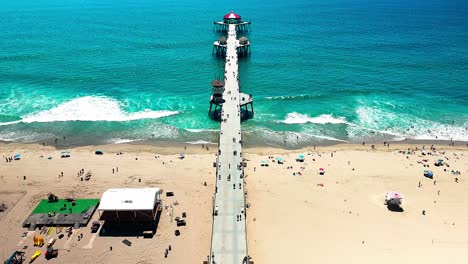 Drone-view-flying-slowly-over-the-fishing-Pier-in-Huntington-Beach-California-with-some-people-walking-around-and-cars-driving-down-PCH,-Pacific-Coast-Highway
