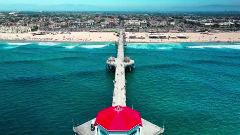 Aerial-view-over-the-Pier-in-Huntington-Beach-California-with-some-people-walking-around-and-a-cool-view-of-the-Pacific-Ocean-and-the-beach-and-surf