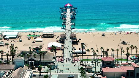 Drone-view-flying-over-the-Pier-in-Huntington-Beach-California-with-some-people-walking-around-and-cars-driving-down-PCH,-Pacific-Coast-Highway