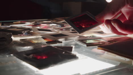 Photographer's-hands-sort-through-a-pile-of-colour-slides-on-a-backlit-table