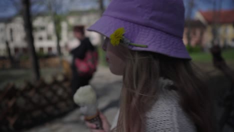 A-girl-with-a-dandelion-in-a-pink-hat-walking-through-the-park-licking-an-ice-cream-cone