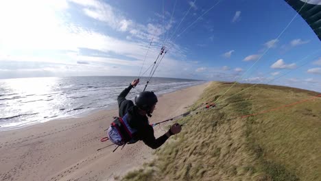 Following-action-shot-of-an-extreme-paraglider-skimming-across-the-dunes-along-a-beach-showing-amazing-skill-and-daring