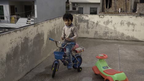 Un-Joven-Paquistaní-Asiático-De-Cinco-Años-Está-Montando-En-Bicicleta-Bajo-La-Lluvia-En-Un-Techo