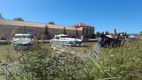Canal-Du-Midi-En-Le-Somail-Francia-Barco-Turístico-Pasando-Por-El-Pueblo-Turístico-En-Una-Cálida-Mañana-De-Verano