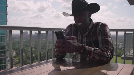 Black-man-with-cowboy-hat-looking-at-phone-smiling-and-laughing