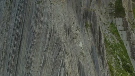 Drone-pedestal-ascends-rock-flysch-sea-cliffs-in-zumaia-spain,-tilt-down