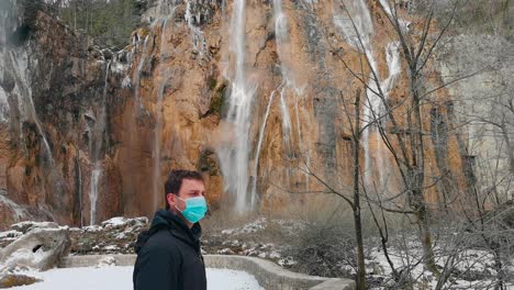 In-a-Croatian-national-park,-a-man-wearing-an-op-mask-symbolizes-pandemic-precautions-amidst-scenic-beauty-with-water-moving-in-background