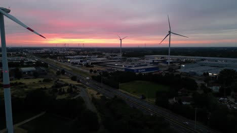 Majestic-sunset-sky-and-silhouette-of-wind-turbines,-highway-and-urban-area,-aerial-view