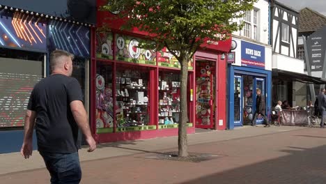 Slow-motion-pedestrians-walking-down-British-Widnes-town-main-street-passing-shops-in-high-inflation-cost-of-living-crisis