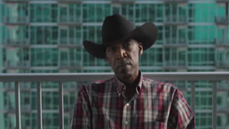 Establishing-shot-of-African-American-male-with-cowboy-hat-sitting-on-balcony-as-wind-blows