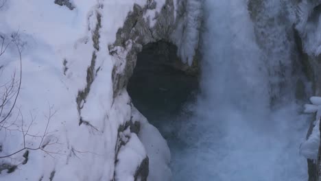 Waterfall-surrounded-by-frozen-snowy-rocks-splashing-and-foaming,-islandic-landscape