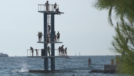 Zoom-out-three-level-high-dive-platform-with-people-jumping-into-the-sea-in-Zadar,-Croatia
