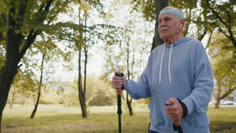 Senior-retired-old-man-grandfather-practicing-Nordic-walking-use-ski-trekking-poles-in-summer-park