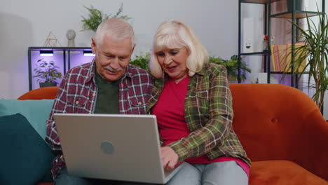 Senior-Großmutter-Großvater-Benutzt-Laptop-Computer,-Tippt-Im-Heimischen-Zimmer-Und-Blickt-Lächelnd-In-Die-Kamera