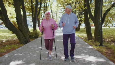 Active-senior-grandparents-training-Nordic-walking-with-ski-trekking-poles,-running-in-summer-park