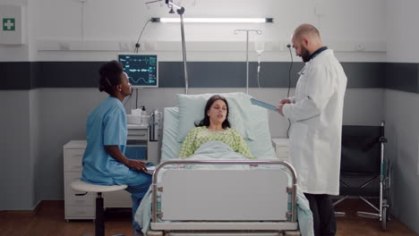 Vorderansicht-Einer-Kranken-Frau,-Die-Auf-Dem-Bett-Liegt,-Während-Eine-Afroamerikanische-Krankenschwester-Röntgenknochen-Analysiert