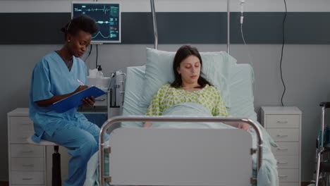 Mujer-Adulta-Enferma-Descansando-En-La-Cama-Mientras-Una-Enfermera-Negra-Analiza-La-Experiencia-En-Enfermedades