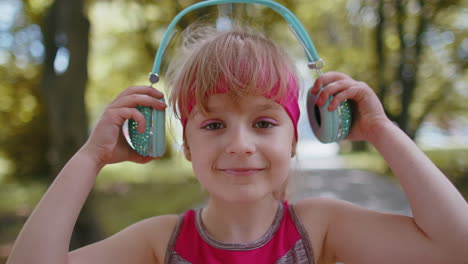 Athletic-fitness-sport-runner-child-girl-wearing-headphones-listening-favorite-music-song-in-park