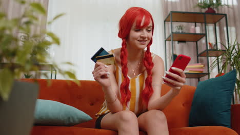 Woman-sit-on-couch-using-credit-bank-card-and-smartphone-while-transferring-money-online-shopping
