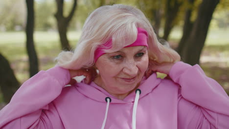 Portrait-of-athletic-senior-sport-runner-woman-training,-listening-music-in-earphones,-wearing-hood