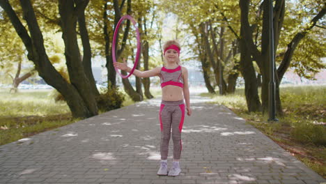 Athletic-fitness-children-girl-training-playing-twisting-Hula-hoop-circle-ring-on-hand-in-park