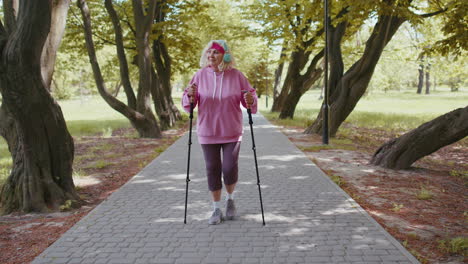 Senior-healthy-retired-woman-grandmother-training-Nordic-walking-in-summer-park,-ski-trekking-poles