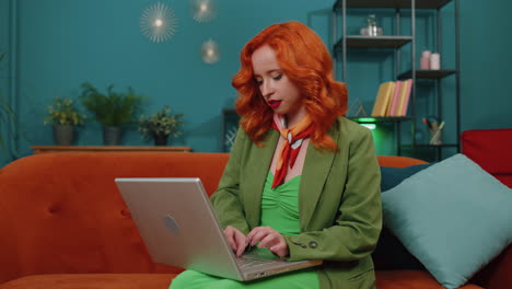 Redhead-young-woman-sitting-on-sofa-closing-laptop-pc-after-finishing-work-in-living-room-at-home