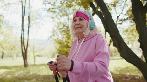 Senior-retired-old-woman-grandmother-practicing-Nordic-walking-use-ski-trekking-poles-in-summer-park