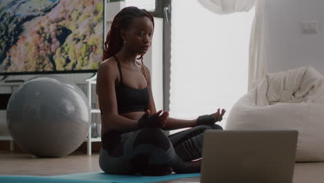 Slim-black-woman-sitting-in-lotus-pose-on-yoga-map-with-closed-eyes