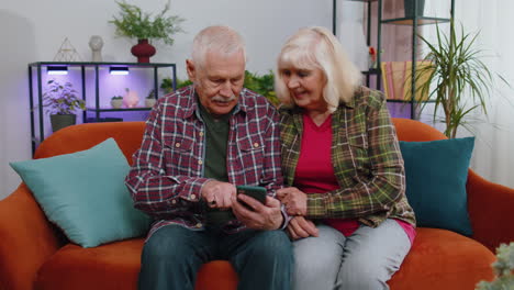 Überglückliche-Großmutter-Und-Großvater-Halten-Ihr-Smartphone-Aufgeregt-über-Den-Gewinn-Einer-Sportwette-In-Der-Mobilen-App-Zu-Hause