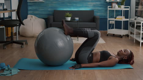 Athletic-woman-with-black-skin-working-abs-on-swiss-ball-in-living-room