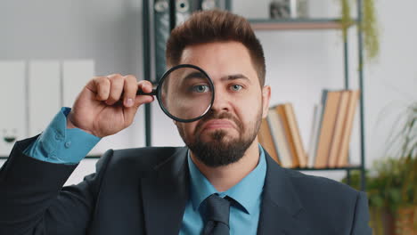 Business-man-holding-magnifying-glass-near-face,-looking-with-big-zoomed-eye,-searching,-analysing