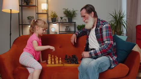 Lächelnder-älterer-Großvater,-Der-Zu-Hause-Schachbrettspiel-Mit-Jugendlicher-Enkelin-Spielt