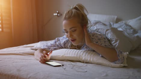 Charming-young-woman-with-ponytail-listening-to-good-music-while-lying-on-comfortable-bed